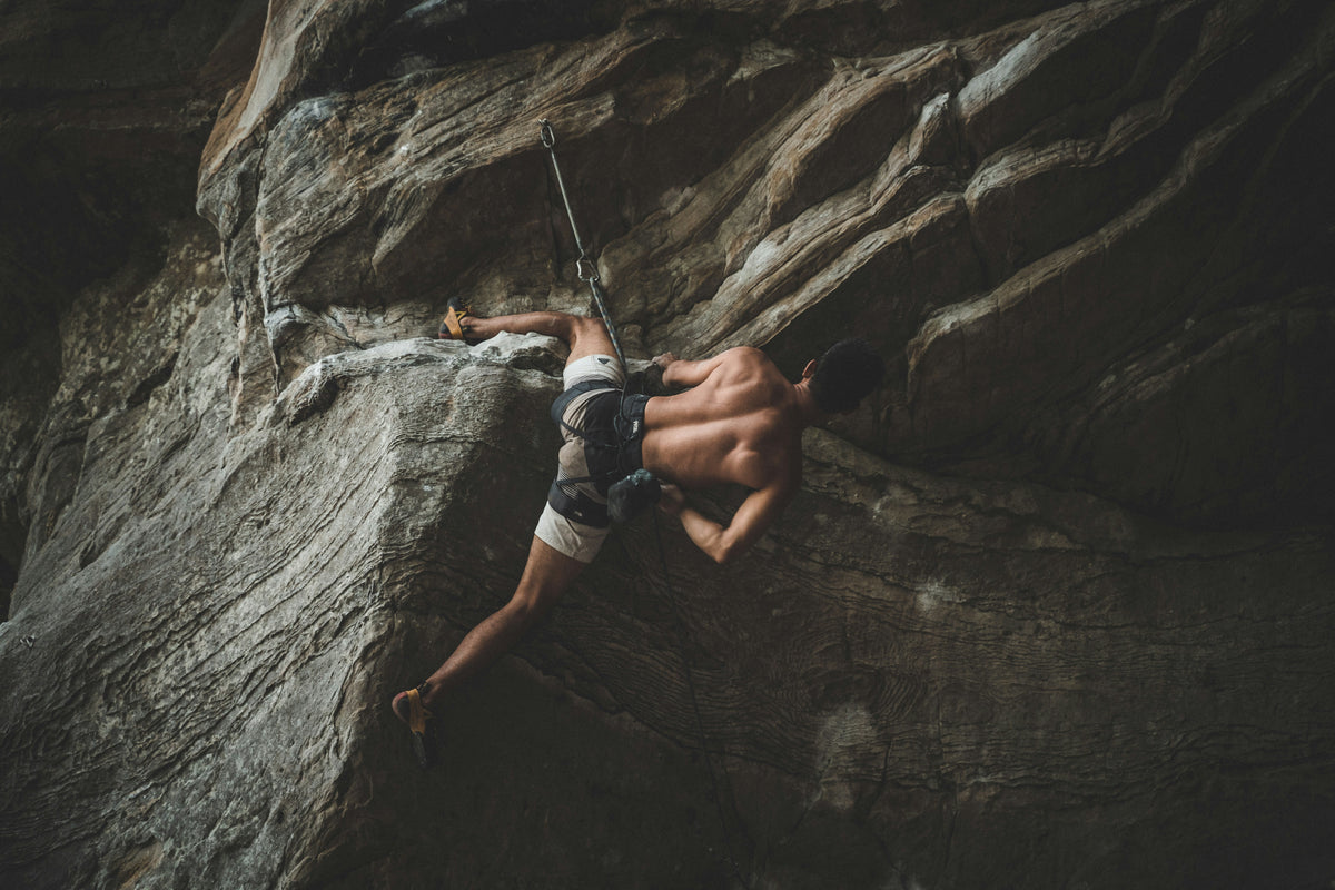 Climber stemmed out on an overhanging sandstone cliff, mid lead climb